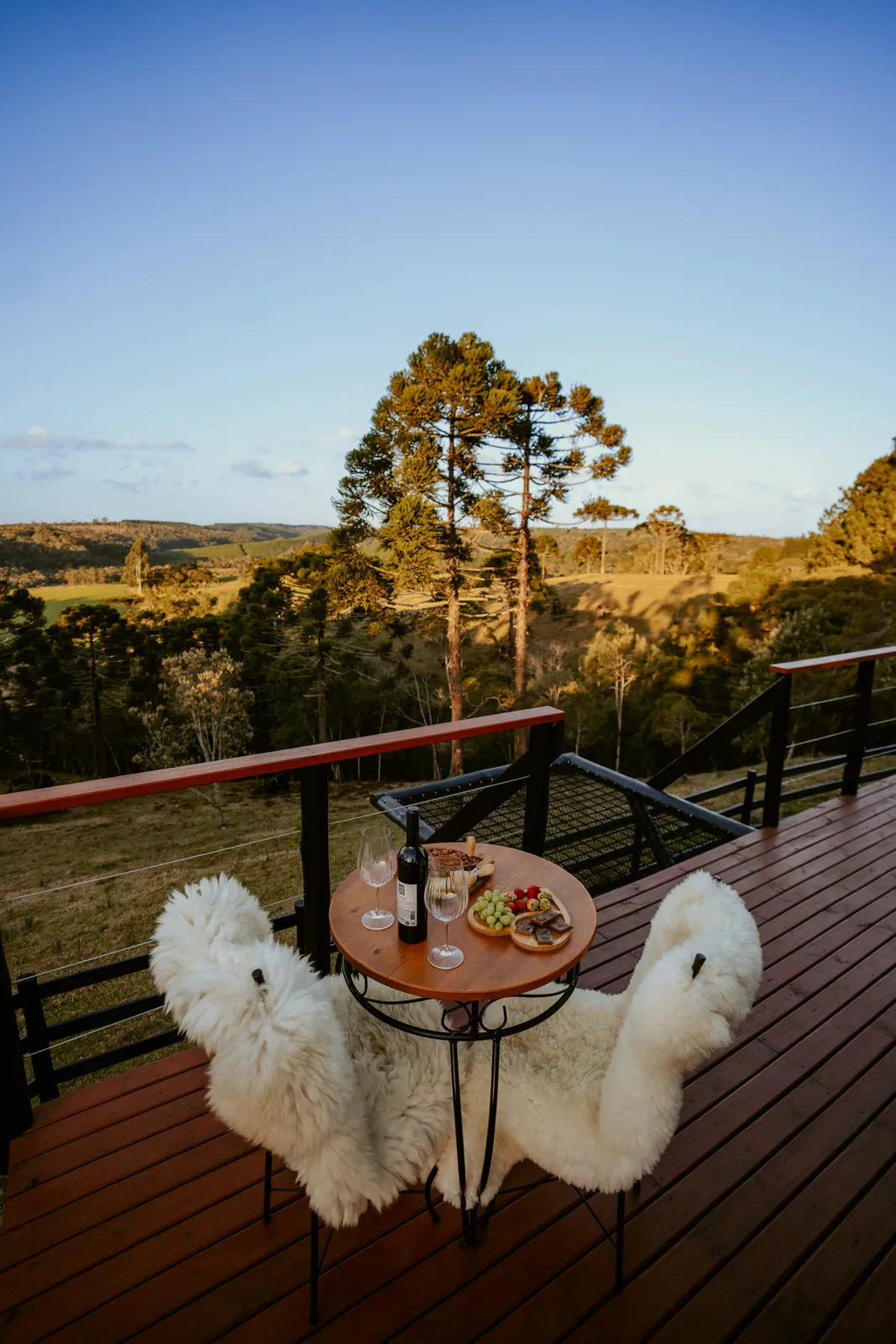 Mesa posta com vinho no deck do chalé, no fim da tarde, com o vale e as araucárias ao fundo