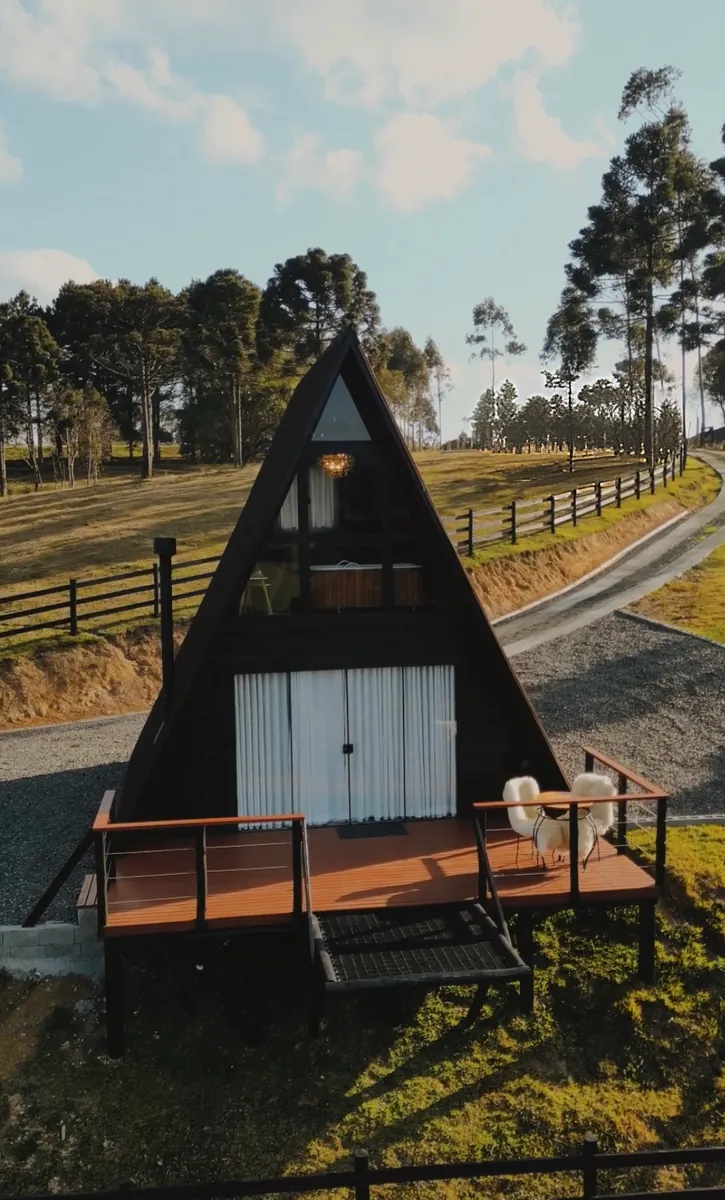 Fachada A-frame do chalé ao entardecer, com o deck e as cadeiras