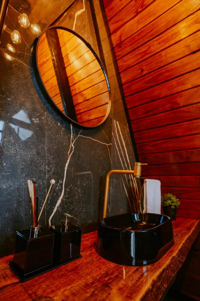 Detalhe do lavabo com cuba preta, torneira dourada e bancada de madeira