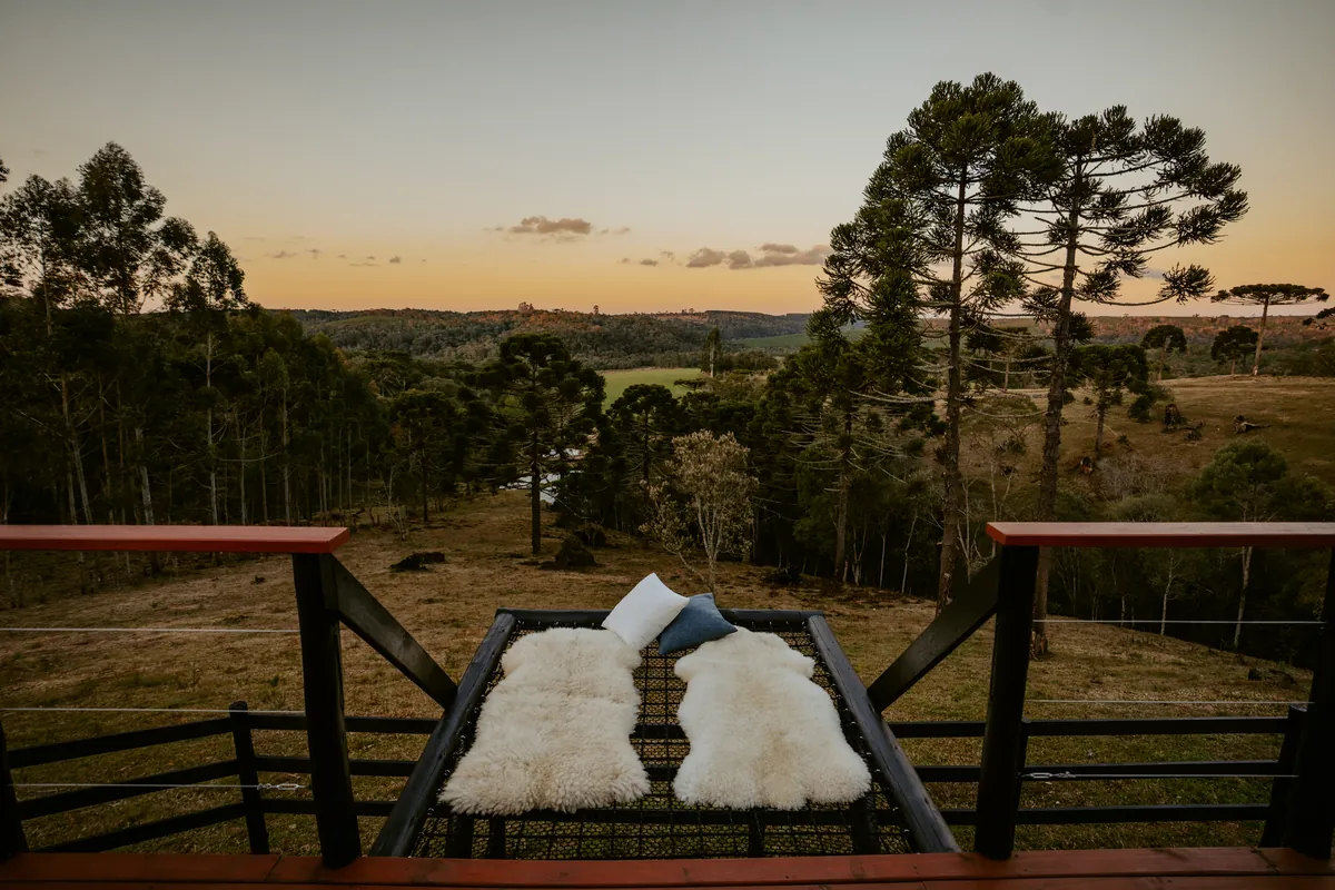 Rede de descanso suspensa no deck, com peles, e o vale ao entardecer