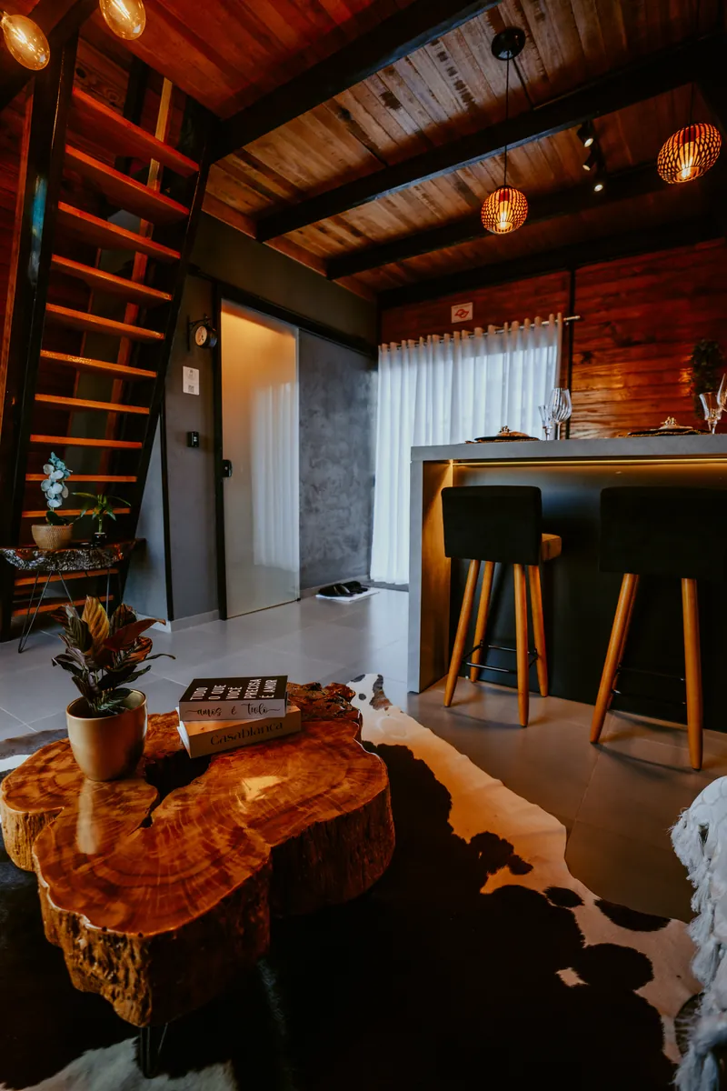 Sala do chalé com escada, mesa de tronco e tapete de couro